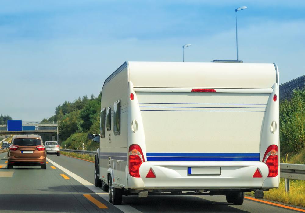 Foto roulotte bianca trainata da auto su autostrada italiana con sfondo verde e cielo azzurro